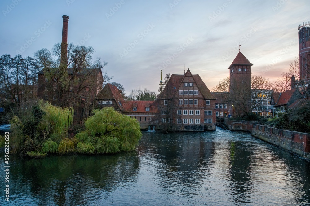 Fototapeta premium Ratsmuhle or old water mill and Wasserturm or water tower on the river Ilmenau in the morning in Luneburg. Germany.