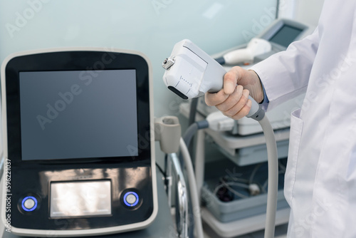 Closeup of young cosmetologist using modern laser machine in beauty clinic