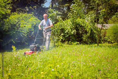 Foto Farmer is mowing lawn in the garden with a petrol lawn mower that smokes