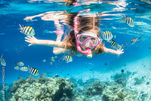 Canvas Print A little girl with mask and snorkel enjoys the underwater life of the tropical o