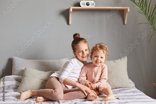 Foto Smiling loving siblings hugging in bedroom happy little girls playing on bed smiling happily having fun in the morning looking at camera positive emotions