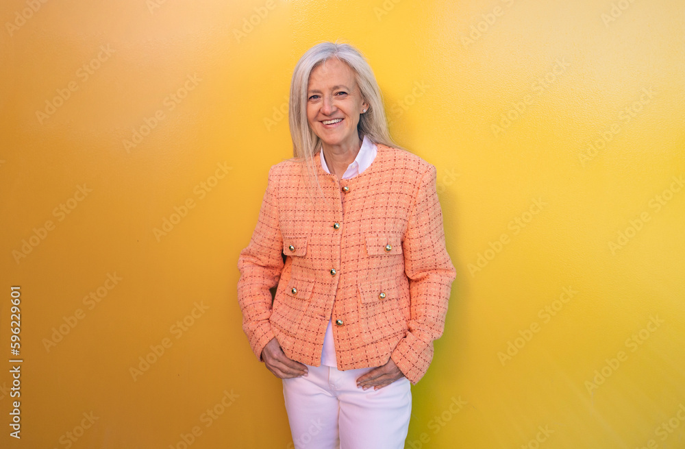Smiling mature woman standing in front of yellow wall Smiling mature woman standing in front of yellow wall