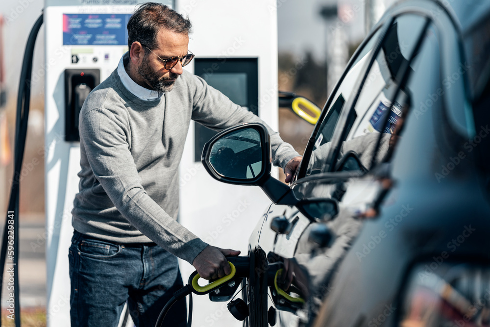 Man charging electric car standing at station Man charging electric car standing at station