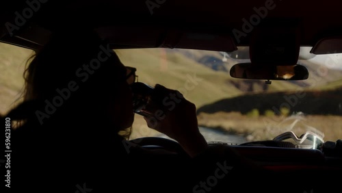 A man sits in a SUV and drinks hot coffee from a thermos. Traveling by off-road vehicle in the mountains. View from the cab of an SUV to the mountains and a mountain river. High