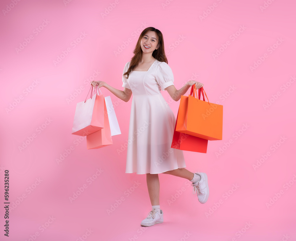 full body image of asian woman holding shopping bag and posing on pink background