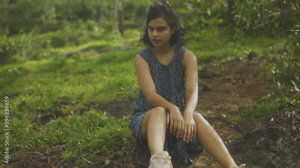 Indian woman sitting on grassy hill in cute blue dress gazes with wonder