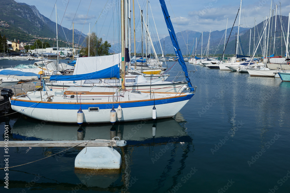 Boats and tall ships moored in a marina in the bay on the lake with mountains in the background