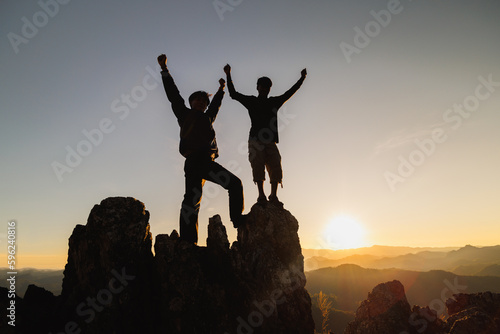 Silhouette of two man with success gesture standing on the top of mountain. business teamwork concept.