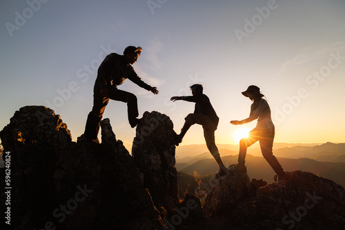Silhouette of Hikers climbing up mountain cliff. Concept of help and teamwork, Climbing group helping each other while climbing up in sunset. Limits of life and Hiking success full.