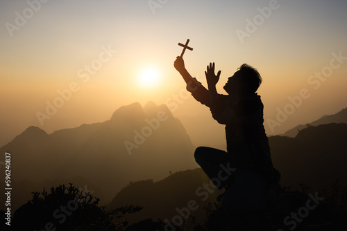 Silhouette of faithful man praying with Christian cross at sunset as concept for religion  faith  prayer and spirituality.