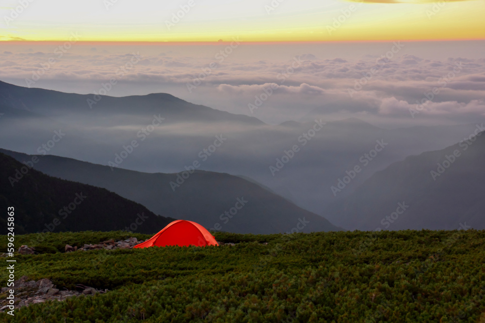 夜明けの雲海を望む山頂に張られたオレンジ色のテント