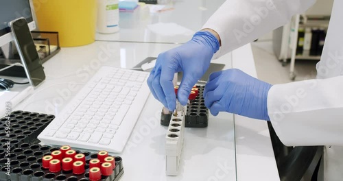 Man working in clinic laboratory. Handheld shot of male medical specialist in uniform preparing blood samples and using analyzing machine during work in lab of modern hospital. photo