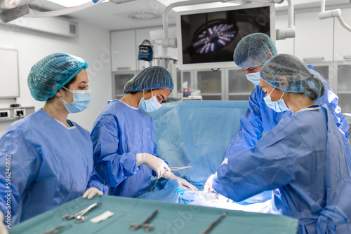 Surgeons doing surgery in operating theatre. Male and female surgeons operating patient. Medical professionals are wearing scrubs.