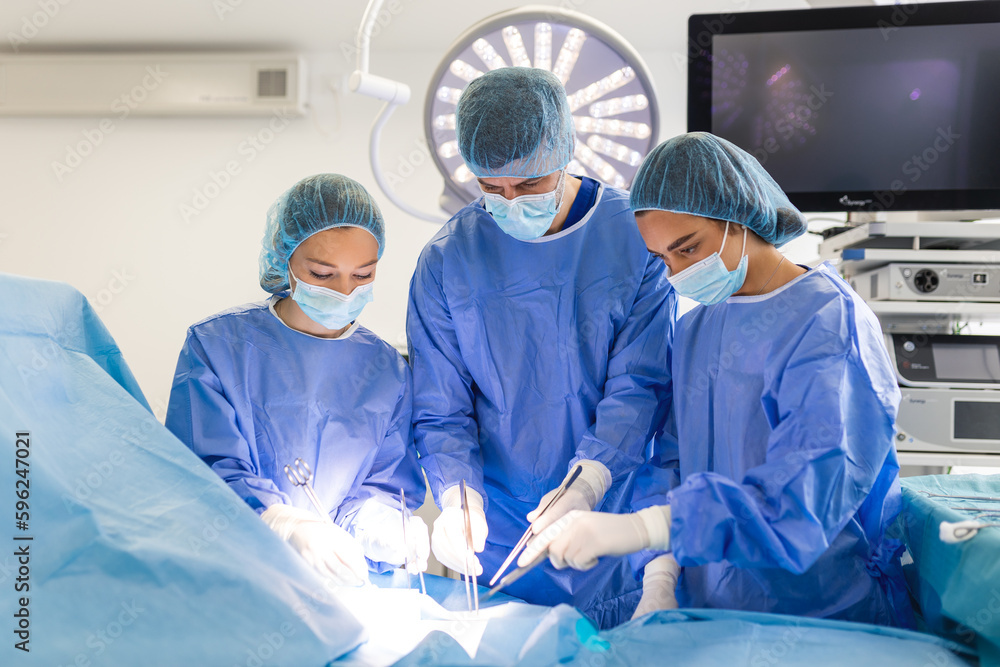 Group of medical team urgently doing surgical operation and helping patient in theater at hospital. Medical team performing surgical operation in a bright modern operating room Group of medical team urgently doing surgical operation and helping patient in theater at hospital. Medical team performing surgical operation in a bright modern operating room