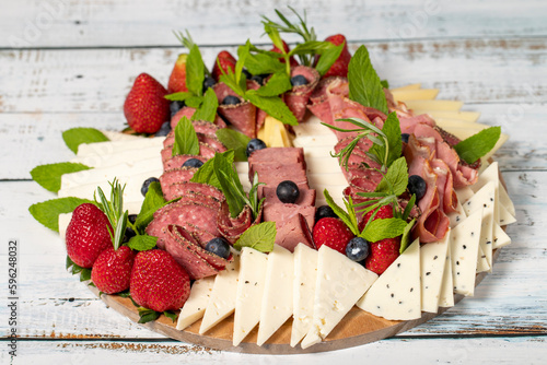 Antipasto set plate. Cold smoked meat plate. Antipasto with ham, prosciutto, salami, blue cheese, mozzarella with blueberries and strawberries. Close up