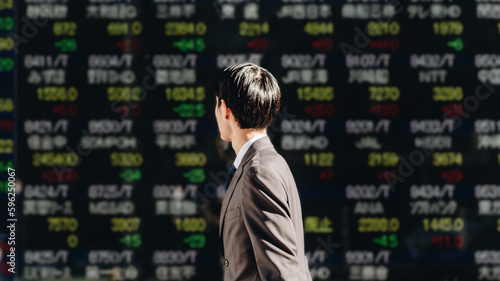 NISAでの株の運用に興味のある若いビジネスマンの男性が屋外の電光掲示板の株価ボードを見るイメージ