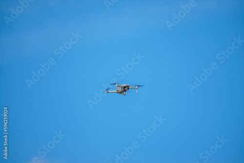 a drone with a high-resolution digital camera flies against a blue sky with clouds, a drone hovers in the air against the sky, a copter hovers in the air
