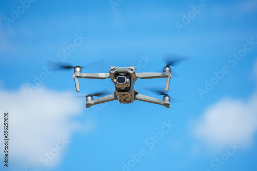 a drone with a high-resolution digital camera flies against a blue sky with clouds, a drone hovers in the air against the sky, a copter hovers in the air © Ruslan Leskov
