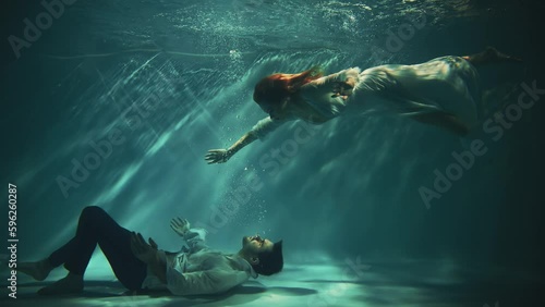 Fantasy gothic romantic couple fall in love man king and woman fashion model posing under water dark blue sea. Wet white dress. Fairy tale sexy girl river nymph swims saves drowning guy. Video shoot photo