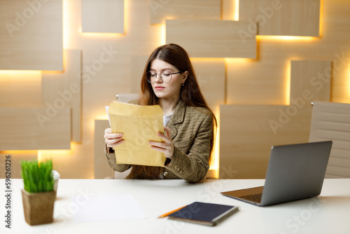 A young businesswoman at the workplace opens a business mail with invoices and reports.