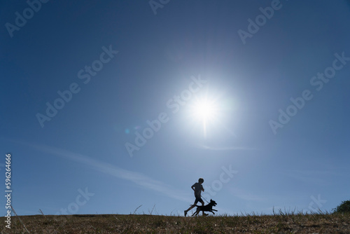 Silhouette of boy and dog running in meadow photo