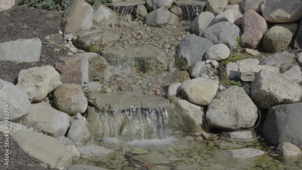 Small handmade garden waterfall made with rocks and pebbles, clear water stream shimmering in sunlight Small handmade garden waterfall made with rocks and pebbles, clear water stream shimmering in sunlight