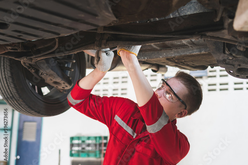 Auto mechanic working in garage, Technician man working in auto service with lifted vehicle, Car repair, and maintenance