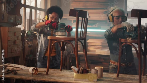 Female carpenters sanding chair in workshop.
