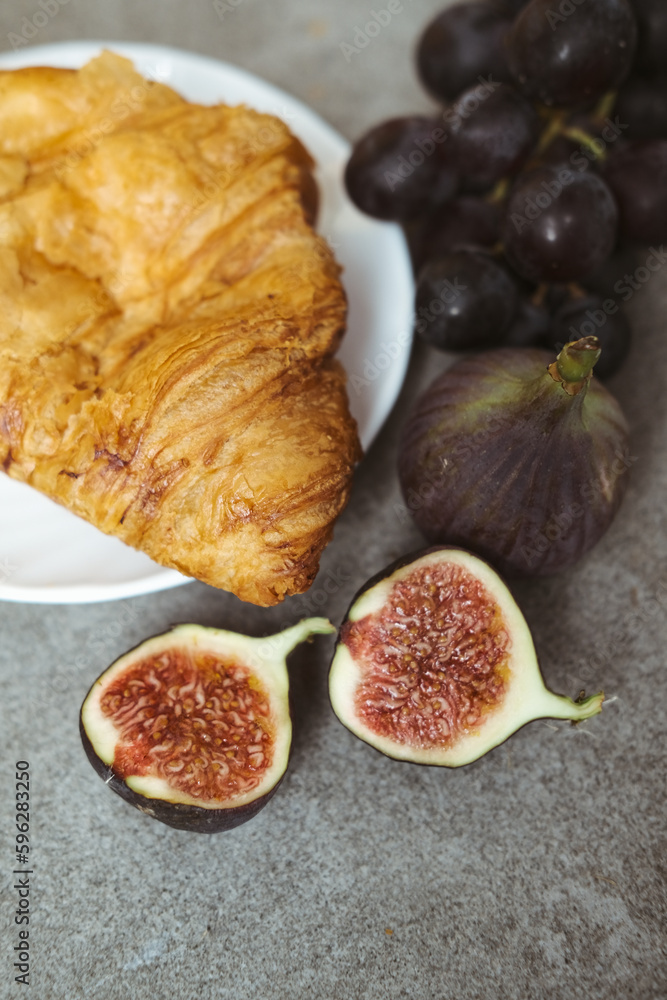 Autumn attributes. Croissant, dark grapes, book and figs on the grey table. Gold October Autumn attributes. Croissant, dark grapes, book and figs on the grey table. Gold October