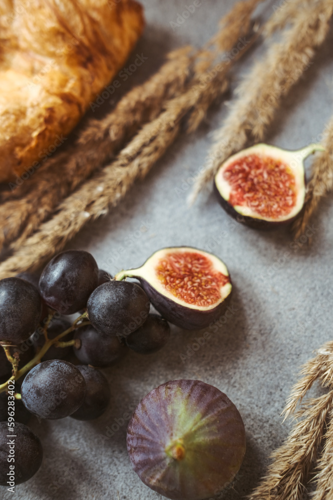 Autumn attributes. Croissant, dark grapes, book and figs on the grey table. Gold October Autumn attributes. Croissant, dark grapes, book and figs on the grey table. Gold October