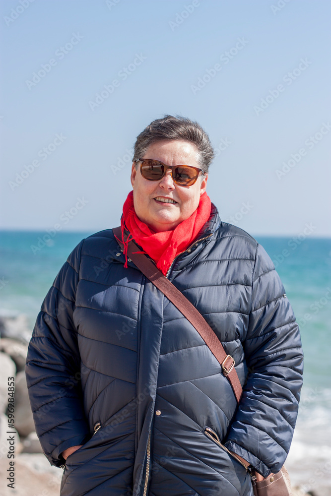 Portrait of adult woman on a sunny winter day on the coast, sunglasses, mediterranean. Walk on the beach in winter.vertical.