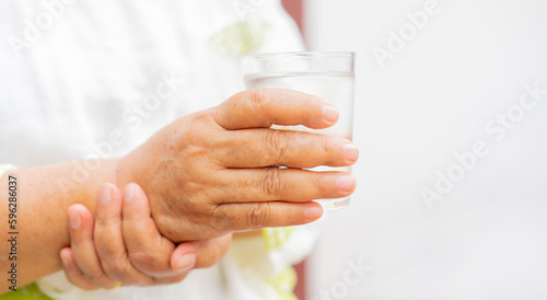 close up senior woman hold on hand to relief shaky symptom while drink water for Parkinson   s disease and chronic illness health care concept