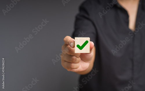 Man holds a wooden cube with a green check mark symbol while standing on a black background