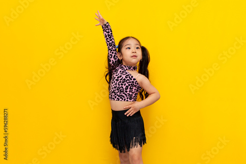 little asian girl in dance outfit dances chachacha on yellow isolated background, korean child dancer trains dance