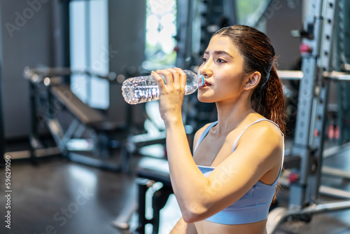 Portrait of tired asian woman in sportswear drinking water from bottle in gym. Female athlete replenishing water balance after fitness workout. being thirsty after practice or training for exercise