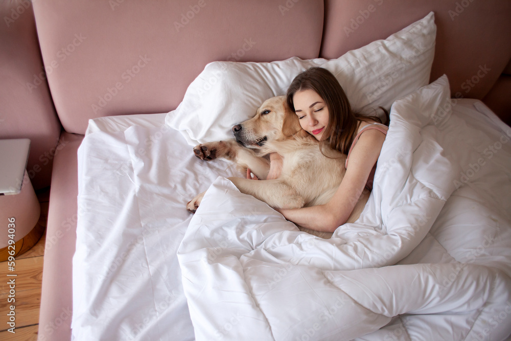 girl in pajamas sleeps in bed with golden retriever dog, woman lies under blanket with pet and dreams