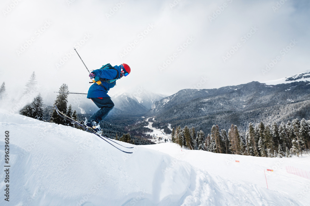 good skiing in snowy mountains. a nice winter day, an incredible ski jump from which a skier jumps against the backdrop of a snowy forest - obrazy, fototapety, plakaty 
