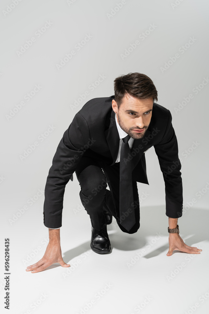 full length of serious and purposeful businessman in low start position on grey background. full length of serious and purposeful businessman in low start position on grey background.