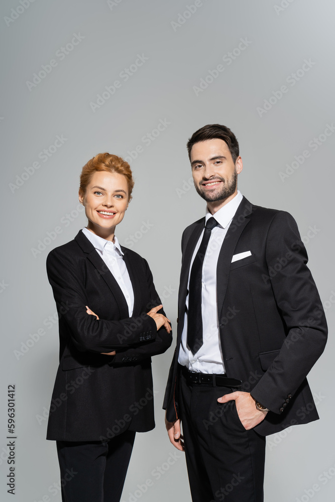 pleased business colleagues in black stylish suits looking at camera and smiling isolated on grey. pleased business colleagues in black stylish suits looking at camera and smiling isolated on grey.