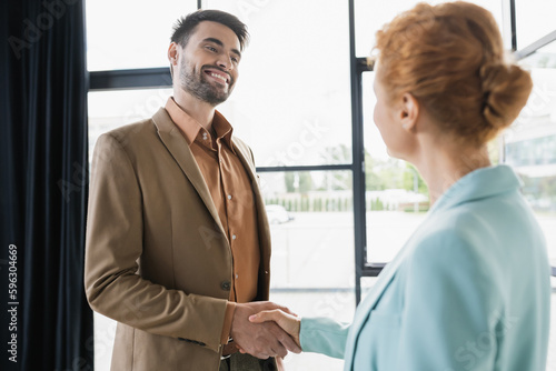 successful businessman smiling and shaking hands with redhead woman in office.