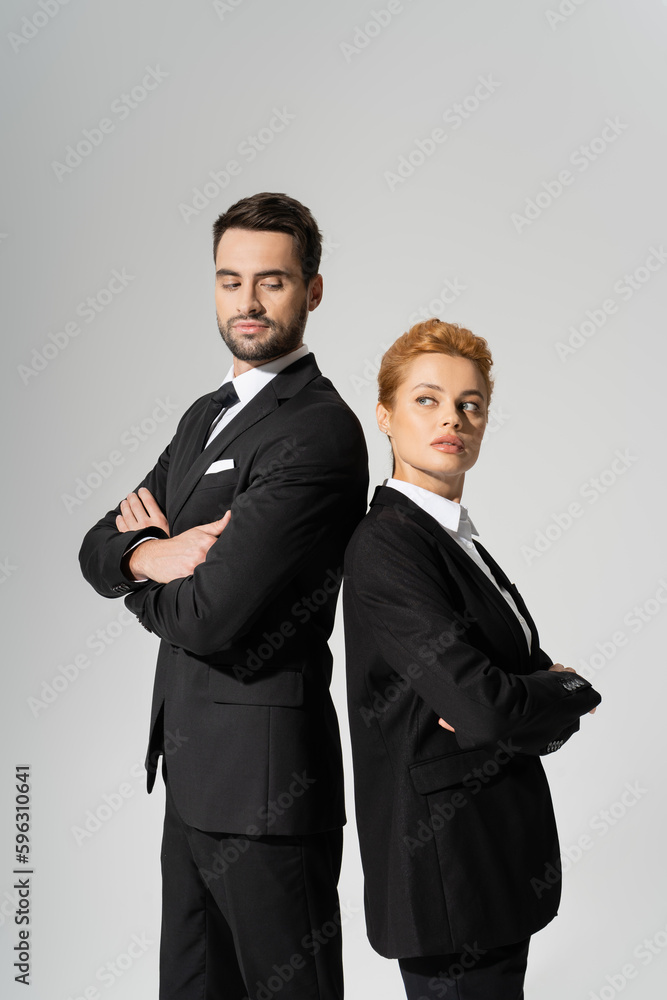distrustful business people in black suits standing back to back with folded arms isolated on grey. distrustful business people in black suits standing back to back with folded arms isolated on grey.
