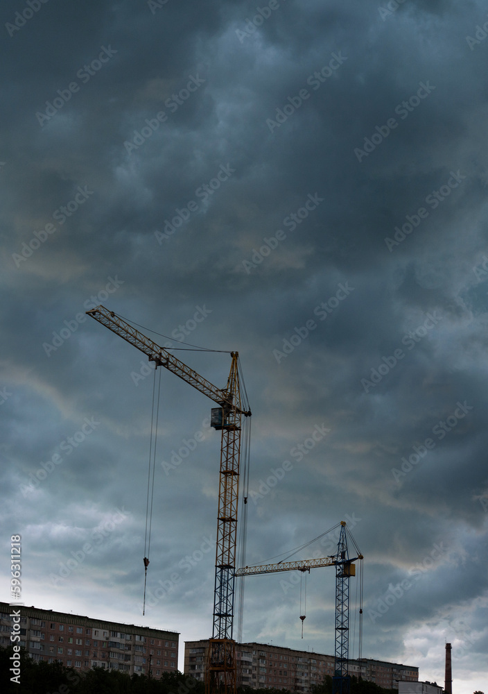 Tower cranes at work under thunderstorm in a district under construction in the suburbs of the city Tower cranes at work under thunderstorm in a district under construction in the suburbs of the city