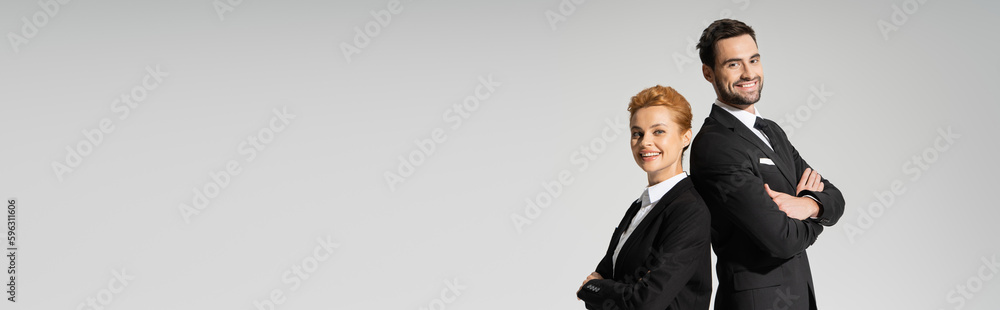 happy managers in black blazers smiling at camera while posing with folded arms isolated on grey, banner. happy managers in black blazers smiling at camera while posing with folded arms isolated on grey, banner.