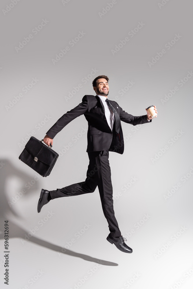 side view of overjoyed businessman with disposable cup and briefcase levitating on grey background. side view of overjoyed businessman with disposable cup and briefcase levitating on grey background.