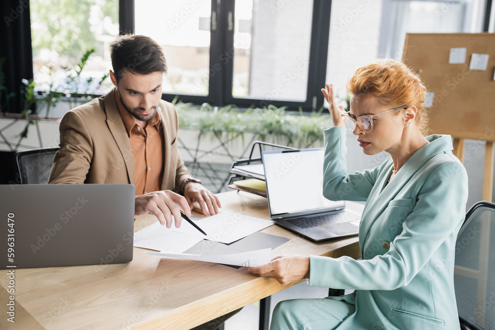 bearded manager pointing at document near displeased businesswoman in office. bearded manager pointing at document near displeased businesswoman in office.