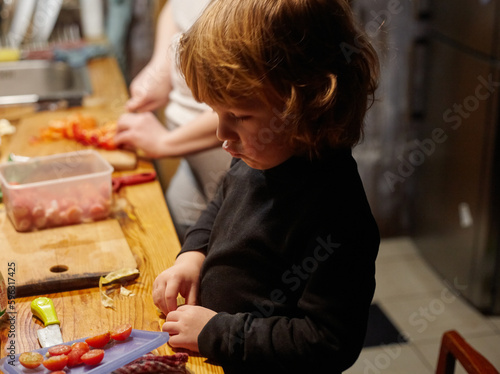 A little boy works in the kitchen, he cuts a tomatoes