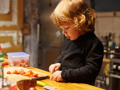A little boy works in the kitchen, he cuts a tomatoes