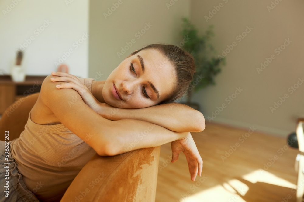 Pretty caucasian student girl resting at home after college, leaning her hands and head on back of sofa in living room, looking aside thinking of something, relaxing her mind and body Pretty caucasian student girl resting at home after college, leaning her hands and head on back of sofa in living room, looking aside thinking of something, relaxing her mind and body