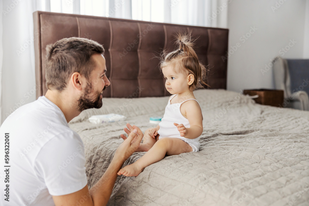 Fototapeta premium A cheerful dad is talking to his baby girl and teaching her how to talk.
