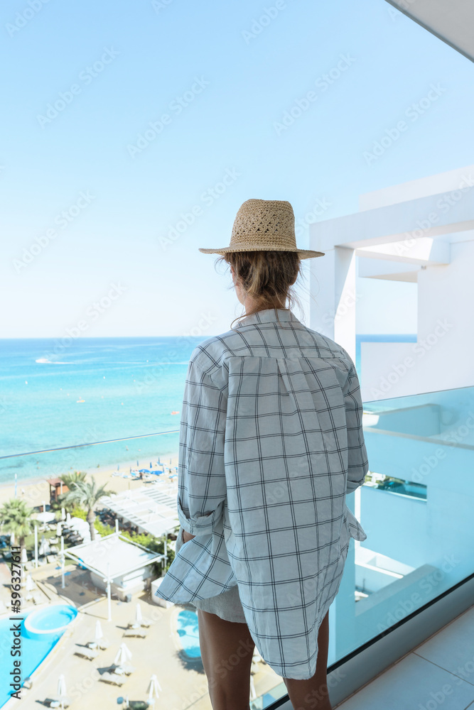 Woman wearing straw hat enjoy view from balcony of beachfront hotel or apartment